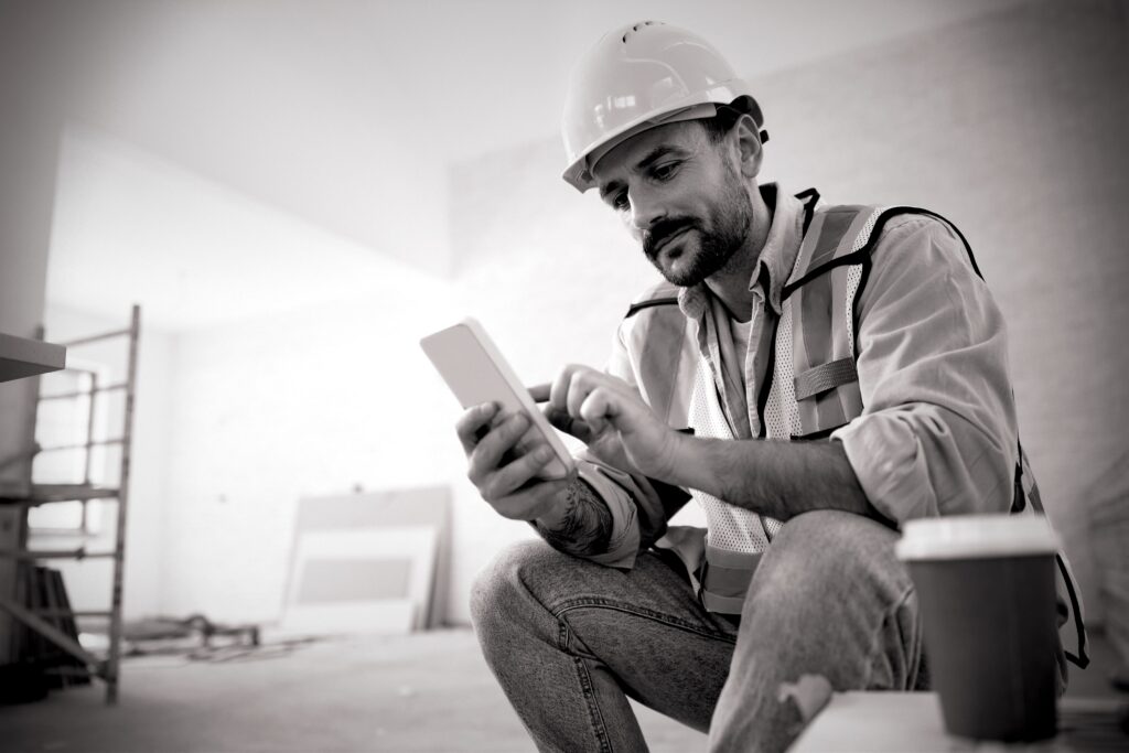 A tradesperson on a break scrolls on his phone while his coffee goes cold.
